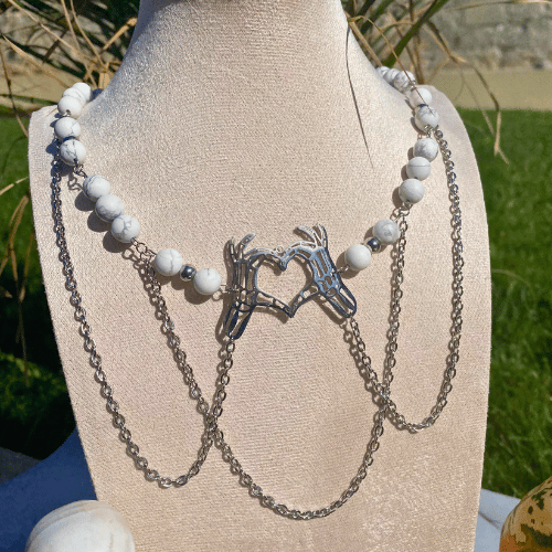Collier sur le thème Halloween avec une breloque représentant des mains de squelette qui font un coeur avec leurs doigts, composé de howlite matte - vue de face