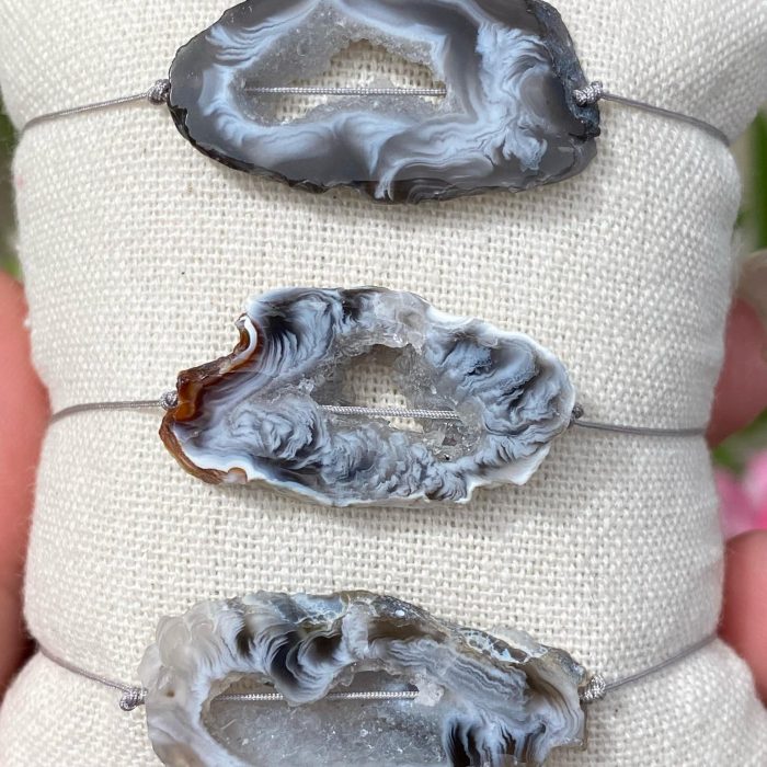 3 bracelets bohèmes sur un coussin beige avec des tranches uniques d'agate de couleur grise, monté sur fil gris, signé Les Merveilles by Pauline.