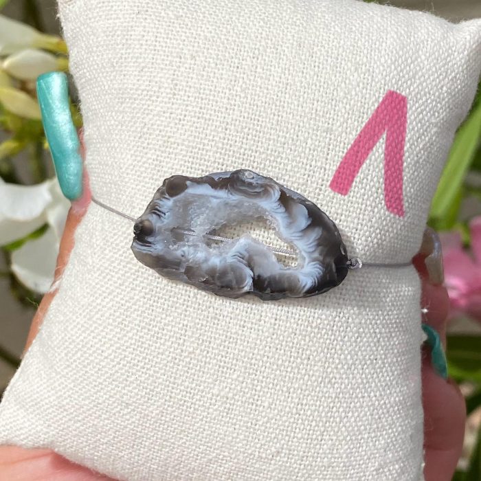 Bracelet bohème n°1 sur un coussin beige avec une tranche unique d'agate de couleur grise, monté sur fil gris, signé Les Merveilles by Pauline.