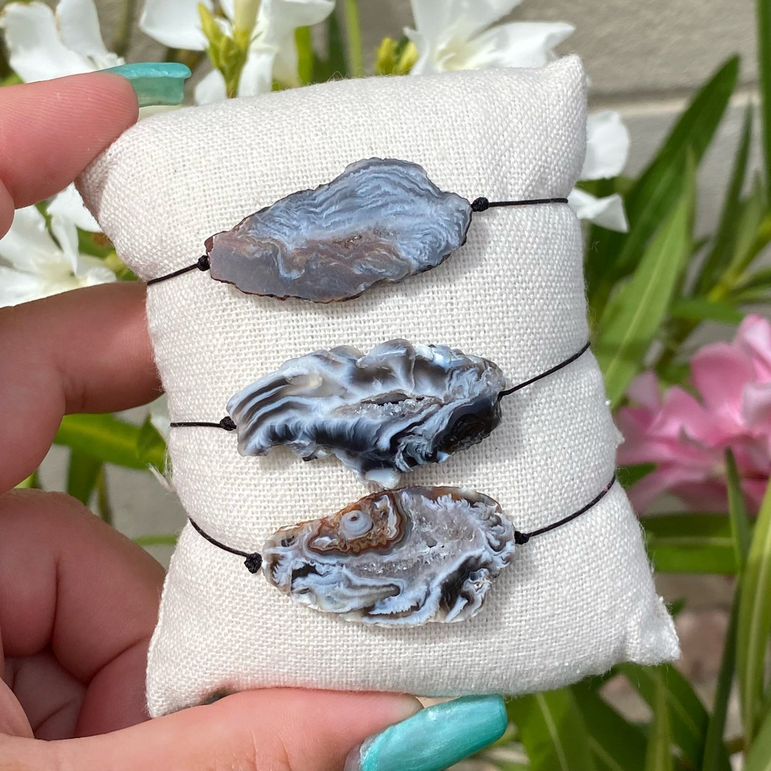 3 bracelets bohèmes sur un coussin beige avec des tranches uniques d'agate de couleur noire, monté sur fil noir, signé Les Merveilles by Pauline.