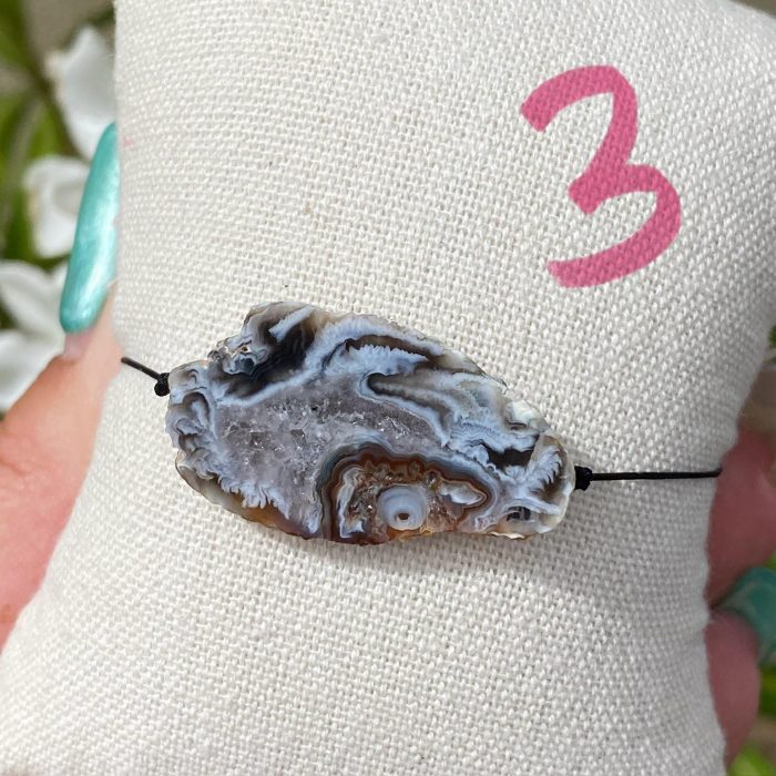 Bracelet bohème n°3 sur un coussin beige avec une tranche unique d'agate de couleur noire, monté sur fil noir, signé Les Merveilles by Pauline.