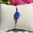 Bracelet bohème en lapis-lazuli (perle centrale rectangulaire et 2 petites perles facettées), avec des apprêts acier doré, posé sur un coussin beige