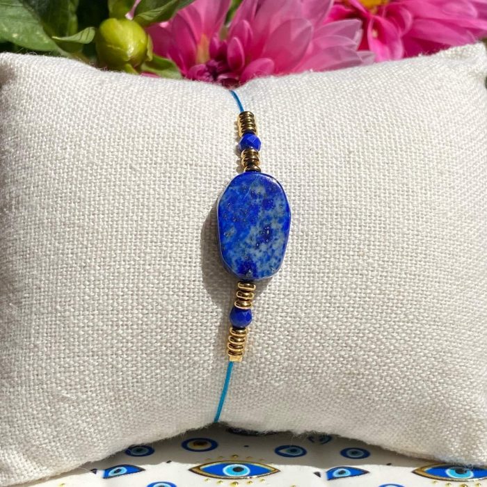 Bracelet bohème en lapis-lazuli (perle centrale rectangulaire et 2 petites perles facettées), avec des apprêts acier doré, posé sur un coussin beige