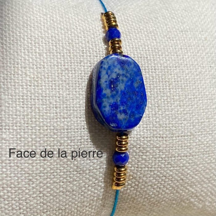 Bracelet bohème en lapis-lazuli (perle centrale rectangulaire et 2 petites perles facettées), avec des apprêts acier doré, posé sur un coussin beige