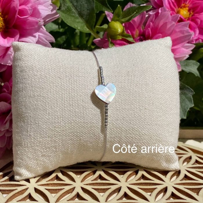 Bracelet bohème composé d'une perle centrale cœur en nacre, avec des perles argentées, posé sur un coussin beige