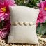 Bracelet bohème composé de 4 yeux de Sainte-Lucie, avec des perles dorées, posé sur un coussin beige