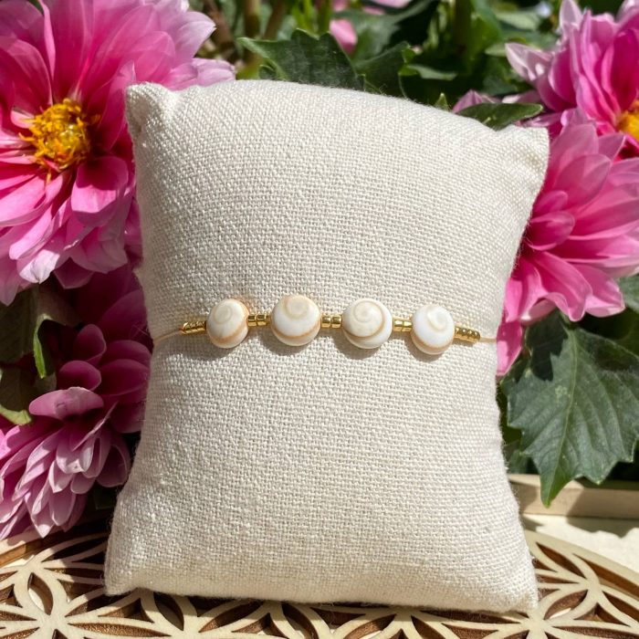 Bracelet bohème composé de 4 yeux de Sainte-Lucie, avec des perles dorées, posé sur un coussin beige