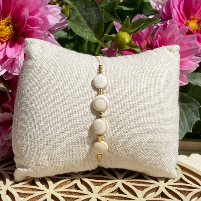 Bracelet bohème composé de 4 yeux de Sainte-Lucie, avec des perles dorées, posé sur un coussin beige
