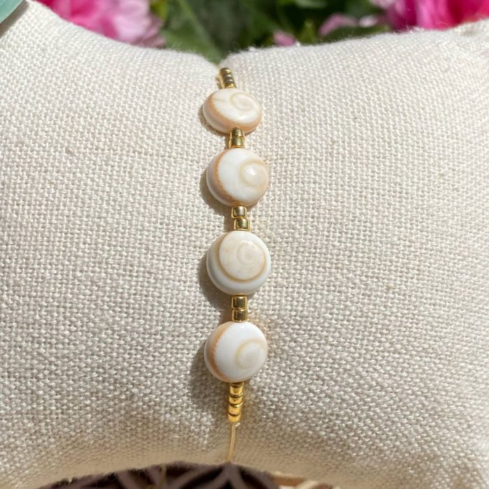Bracelet bohème composé de 4 yeux de Sainte-Lucie, avec des perles dorées, posé sur un coussin beige