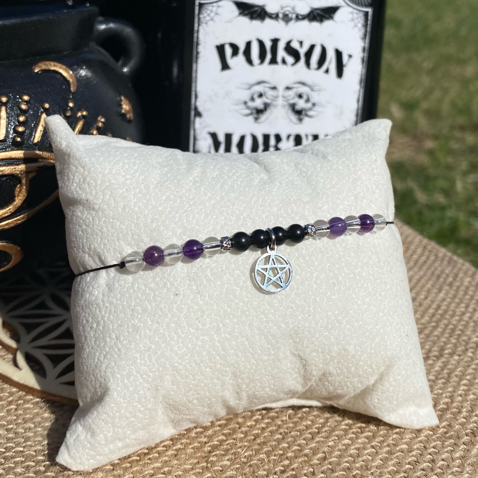 Bracelet inspiré de la Grand-mère Addams, composé d’améthyste, de cristal de roche et d'obsidienne noire, avec breloque pentacle argentée. Création artisanale ésotérique symbolisant la sagesse, la magie et la transmission des savoirs anciens. Inspiré par la série Netflix Wednesday et le film La famille Addams.