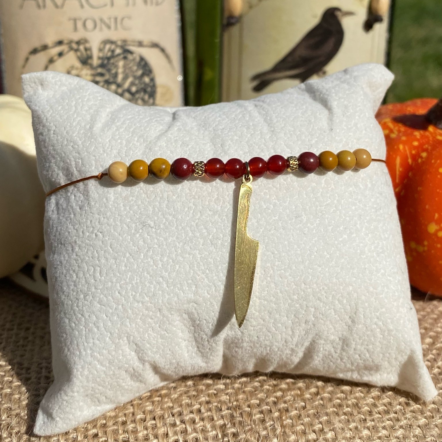 Bracelet fait main inspiré du personnage Chucky, composé de jaspe mokaïte et de cornaline, orné d’une breloque couteau doré, bijou artisanal Halloween en pierres naturelles.