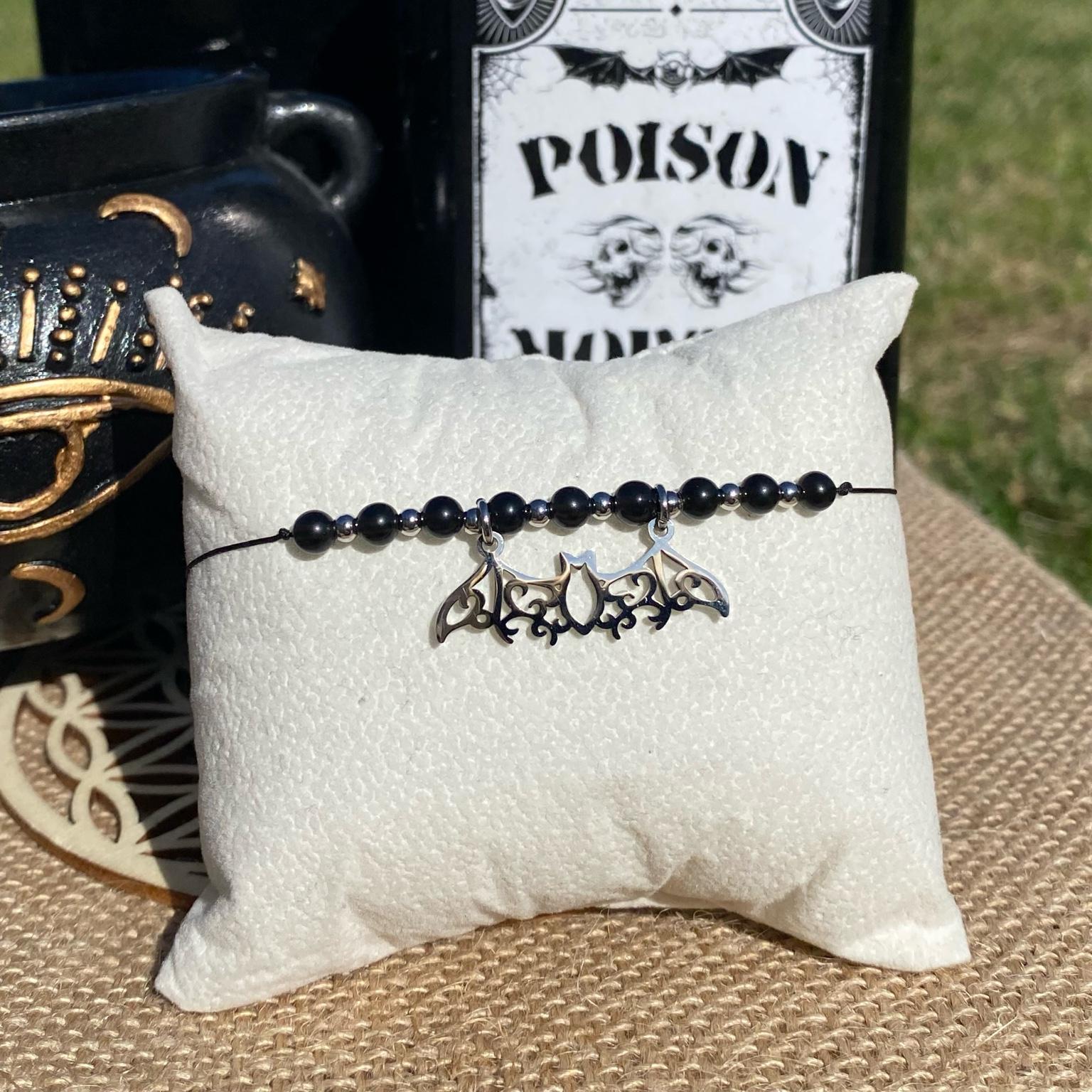 Bracelet inspiré de Mercredi Addams, fait main en obsidienne noire, avec breloque chauve-souris argentée en acier inoxydable. Bijou sombre et raffiné, symbole de protection, d’ancrage et d’indépendance. Inspiré par la série Netflix Wednesday et le film La famille Addams