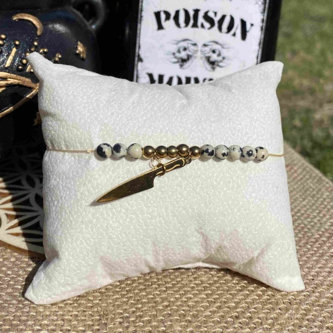 Bracelet inspiré de Puglsey Addams, en jaspe dalmatien, apprêts dorés en acier inoxydable et une breloque couteau doré. Inspiré par la série Netflix Wednesday et le film La famille Addams.